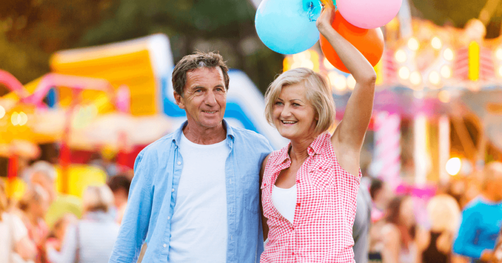 Older couple walking with balloons and festival rides behind them.